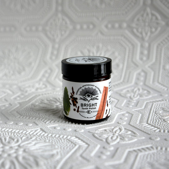 A jar of Bright Tooth Polish with a black lid and white label, placed on a textured white surface with a matching embossed background.