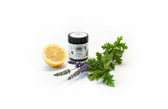 Fresh cream deodorant with a black lid and white label, styled with a halved lemon, lavender sprigs, and green herbs on a clean white background.