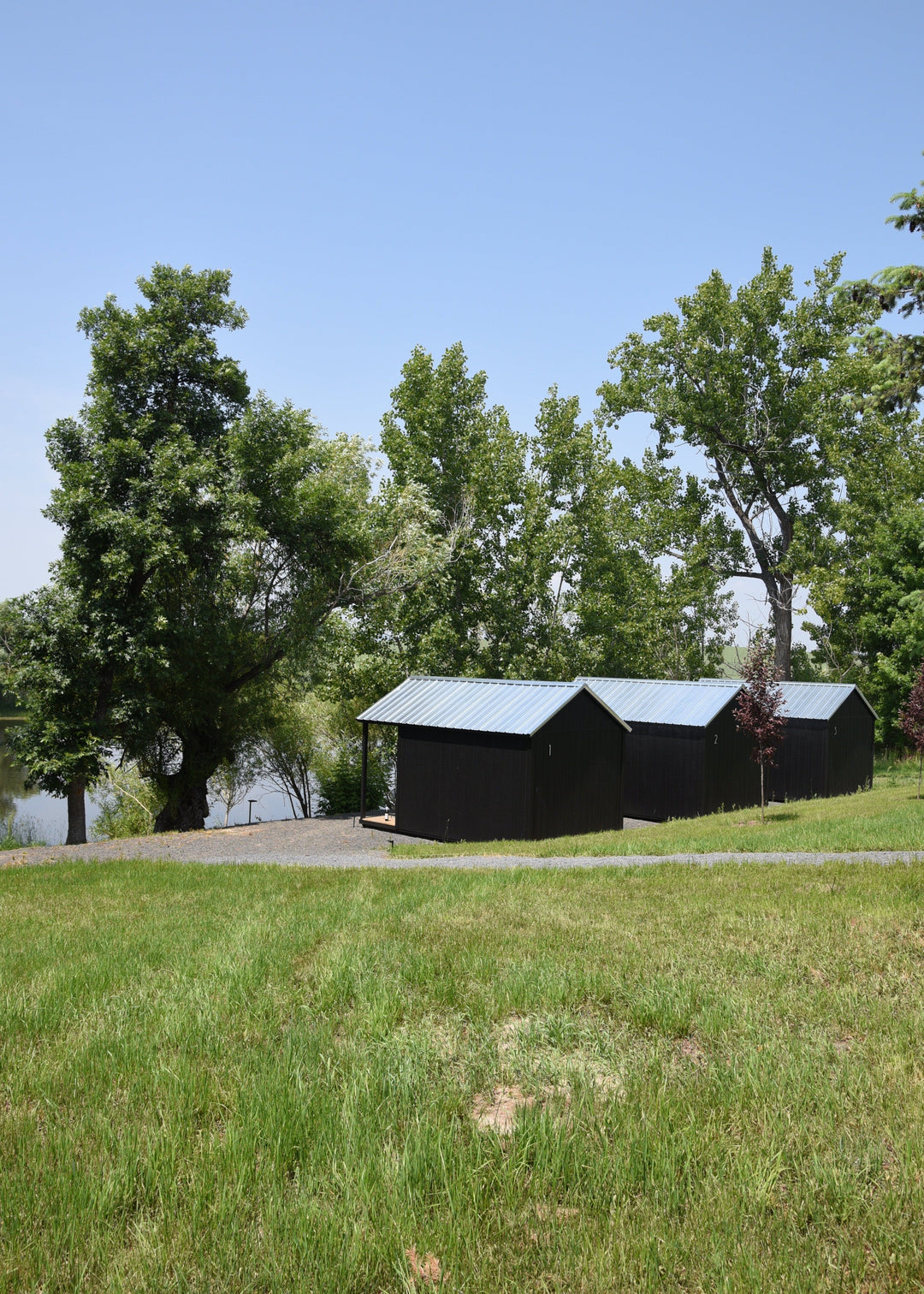 Row of black pond side cabins in a grassy field