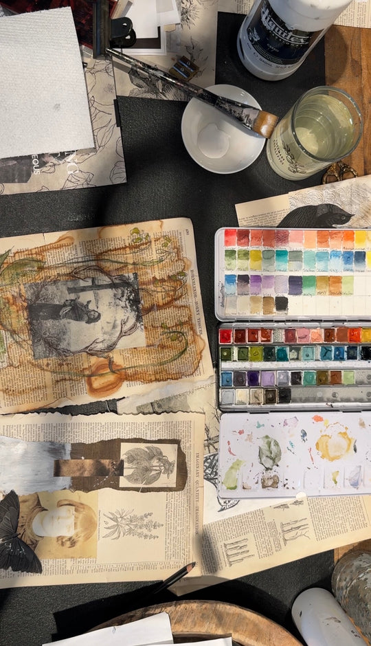 Artistic workspace with watercolor paints, brushes, and sketches on a table.